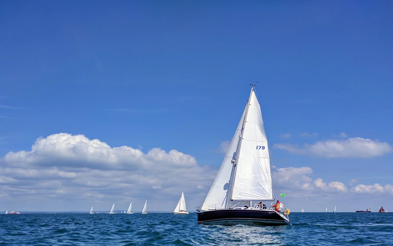 A cruising-size sailing yacht with a white mainsail and headsail, sail number 179, heeling on blue water off the Isle of Wight, with more yachts on the horizon
